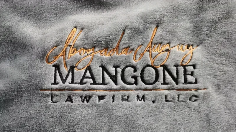Gold metallic thread embroidery of Mangone Law Firm logo on gray sherpa fleece