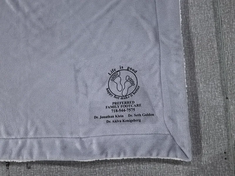Small fine-text heat transfer logo for a footcare clinic on light gray blanket