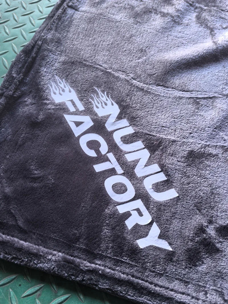 NUNU FACTORY white heat transfer logo with flame details on dark gray blanket